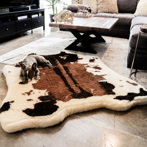 a french bulldog in a modern living room with a small wooden table , black drawers and a grey L shaped couch laying on a cowhide printed fluffy dog bed 
