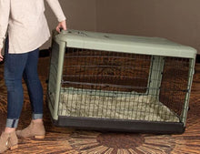 a woman wearing jeans dragging a sage colored dog crate from the floor with modern design