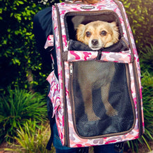 A cute dog inside of a pink camo colored pet carrier being carried by a woman on a sidewalk