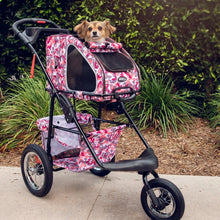 a cute dog riding a pink camo dog stroller inside a dog carrier next to some tall grasses