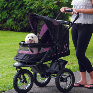 a woman walking her dog in a pink dog stroller in the park