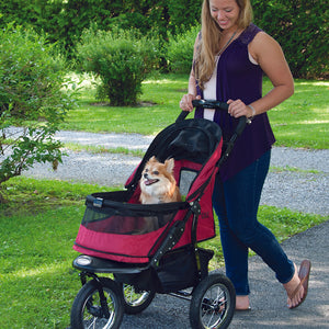 a woman walking her dog on a rugged red dog stroller in the park