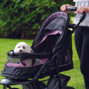 a close up image of a woman walking her dog in a pink dog stroller in the park