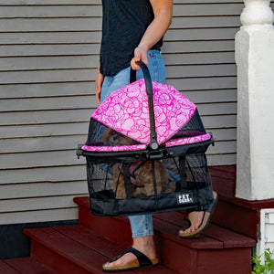 a woman carrying a pink floral designed dog carrier down the brown wooden stairs
