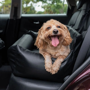 a fluffy dog sticking his tongue out laying on a black leather car dog bed 
