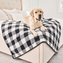 a close up image of a labrador retriever laying on a black and white checkered pattern dog blanket at the edge of a white cozy bed 