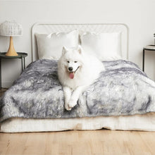 a samoyed laying on a white bed with white and grey fluffy dog blanket in a modern bedroom with bedside table and lamps