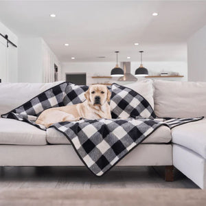 a labrador retriever laying on a black and white checkered pattern dog blanket on an L shaped white couch in an all white modern living room