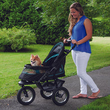 a woman walking her dog in a green dog stroller in the park