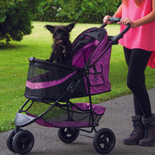 a woman walking her dog in a pink colored dog stroller in the park