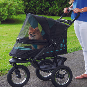 a close up image of a woman walking her dog inside a green dog stroller in the park