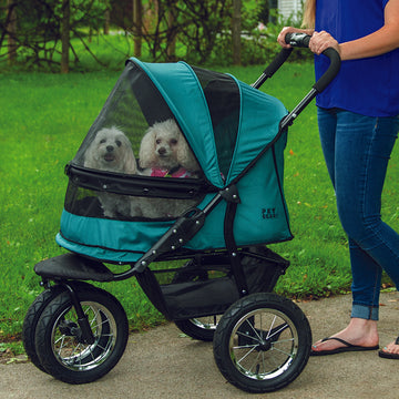 a woman walking her dog inside a pine green dog stroller on the sidewalk