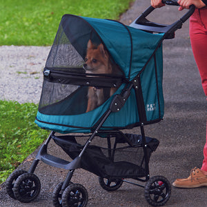a woman walking her tiny dog inside a green  dog stroller in the park