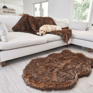 a labrador retriever laying on a brown furry dog blanket on a white L shaped couch near the window and a brown furry dog bed on the floor 