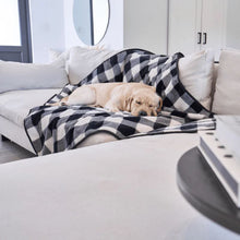 a labrador retriever sleeping on the white couch on a black ang white checkered dog blanket in an all white room setting 