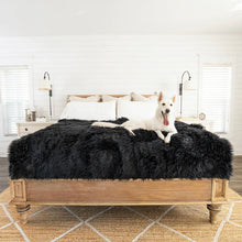 a white samoyed laying on a black furry dog blanket on top of a wooden bed in a modern bedroom with bedside drawers and lamps
