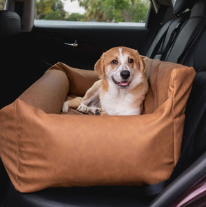 a cute little puppy laying on a brown car dog bed at the back seat of a car with black leather seats