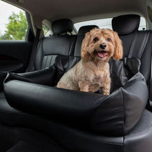 a cute fluffy dog sitting on a black leather car dog bed in the back seat of a car 