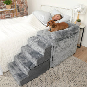 a woman sleeping ona a white bed next to her dog on a grey fluffy bedside dog sleeper 