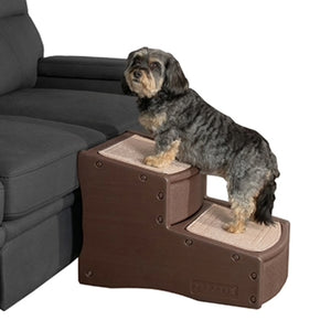 a fluffy tiny dog standing on a two step brown dog stair next to a grey couch with white background