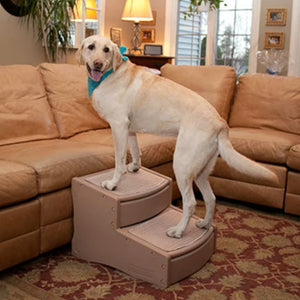 a big white dog standing on a tan two step dog stair next to a brown couch in the living room