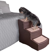 a tiny fluffy dog standing on a chocolate colored three step dog stair next to a grey bed with white bacgroun