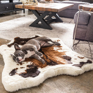a french bulldog in a modern living room with a small wooden table , black drawers and a grey L shaped couch laying on a cowhide printed fluffy dog bed