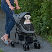 a cute white fluffy dog inside a grey stroller being pushed by a woman on the path walk next to some green leafy plants