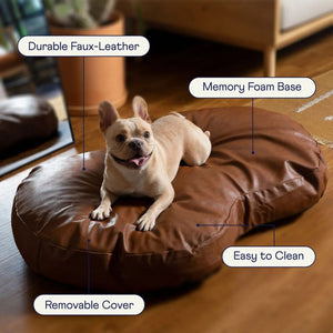 a french bulldog laying on top of a brown leather dog bed 