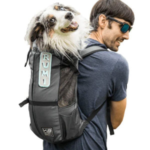 a man in grey wearing sunglasses carrying his dog on his back in a black dog backpack carrier