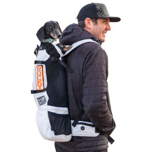 a man wearing a cap carrying his dog on his back inside a white dog backpack carrier  with black side pockets