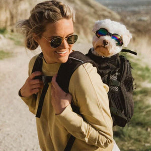a lady carrying her dog on her back in a black dog backpack carrier wearing sunglasses on hiking 