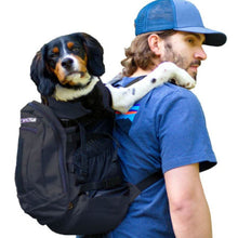 a man wearing blue cap carrying his dog on his back in a  black dog backpack carrier