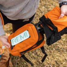 top view image of a lady next to her dog holding an orange dog backpack harness 