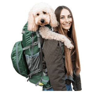 a happy woman carrying her dog in her back in a green dog backpack carrier 