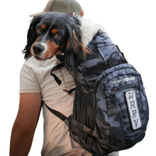 a lady wearing white carrying her dog on her back in a camo dog backpack carrier with side pockets