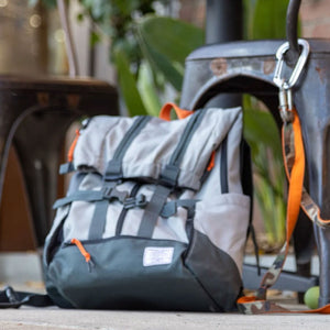 Close up image of a grey dog backpack carrier sitting on the floor next to a steel chair and an orange leash 