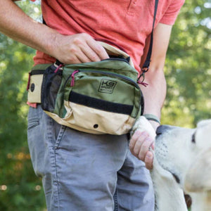 a close up image of a man wearing a hip bag with his hands inside it and  his other hand holding a dog 