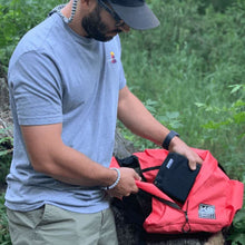 a man on the woods putting a booster block inside an orange backpack on a dead tree