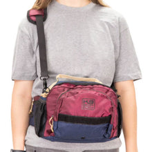 a woman wearing grey shirt wearing a red shoulder and hip bag 