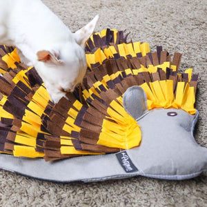 Close up image of a white dog playing on a hedgehog shaped snuffled pad on the ground 