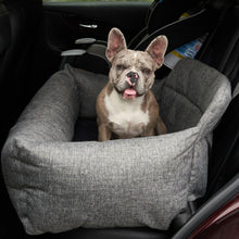 A french bulldog sticking his tongue out sitting on a grey dog bed in the car seat