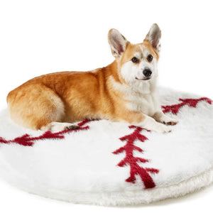 A corgi laying on a round white baseball shaped dog bed 