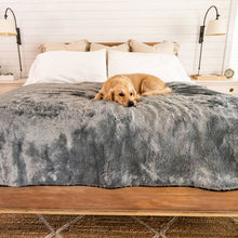 A golden retriever on bed with waterproof grey dog blanket and white and  brown pillows on the background and a white table lamp next to an alarm clock