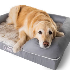 A golden retriever resting on a rectangular gray bolster bed in a white with brown accented fur bed facing front