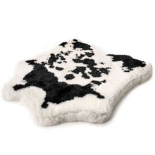 A soft furry curved dog bed with a black and white cow hide pattern