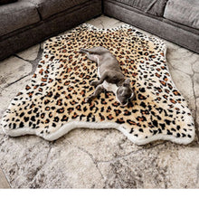 A tiny French bulldog on the floor next to a grey sofa laying on a soft furry dog bed with cheetah pattern