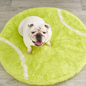 A top view of a white english bulldog sitting on a furry tennis ball shaped dog bed on the floor
