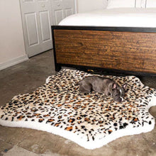 A French Bulldog laying on a big curved dog bed with cheetah hide pattern  next to a wooden bed with white foam and pillows beside a door on a modern room