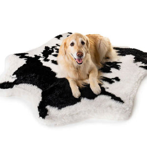 A Golden Retriever laying on a soft furry curved dog bed with a black and white cow hide pattern